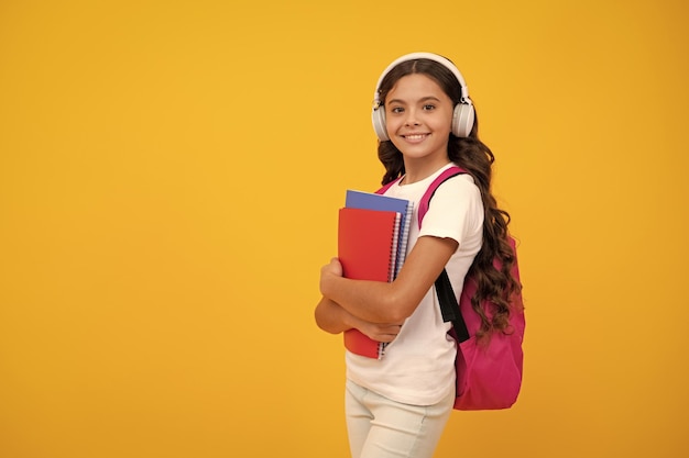 Colegiala estudiante adolescente estilo de vida chica en auriculares sostienen libros sobre fondo de estudio aislado amarillo Concepto de educación escolar y musical