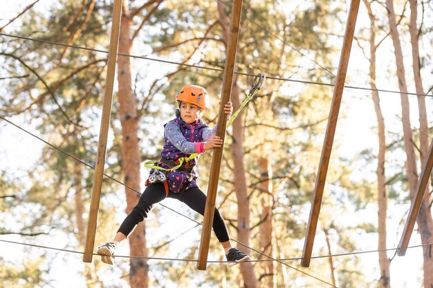 Colegiala feliz disfrutando de la actividad en un parque de aventuras de escalada en un día de otoño