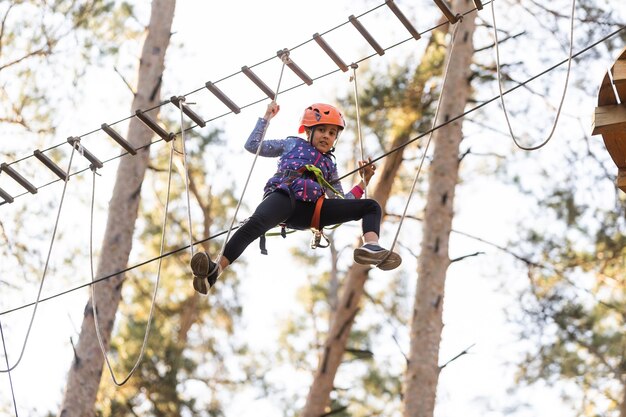 Colegiala feliz disfrutando de la actividad en un parque de aventuras de escalada en un día de otoño