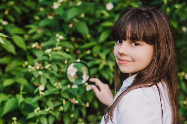 Colegiala feliz examina las flores bajo una lupa