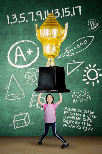 Colegiala feliz levantando un gran trofeo en el aula