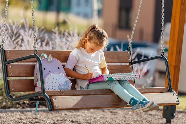 Colegiala feliz con una mochila sonriendo y leyendo notas en cuadernos