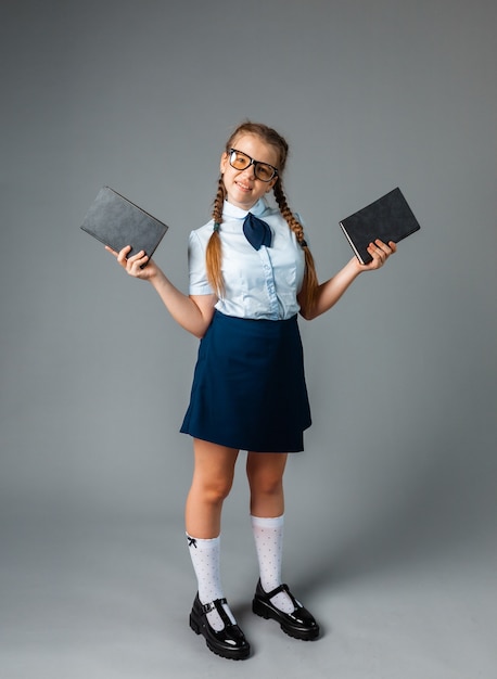 Colegiala feliz de pie con el libro en las manos, aislado sobre fondo gris