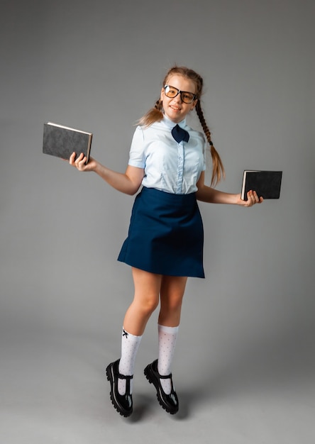 Colegiala feliz de pie con el libro en las manos, aislado sobre fondo gris