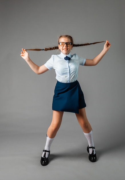 Colegiala feliz de pie con el libro en las manos, aislado sobre fondo gris