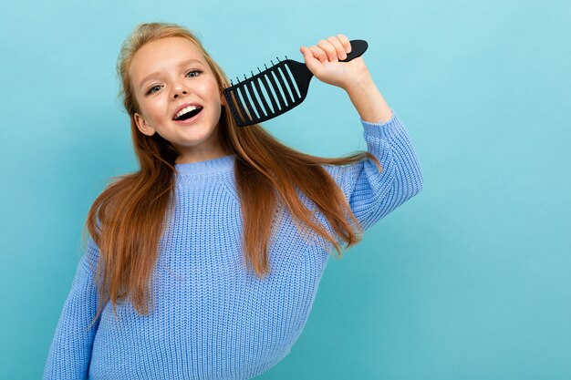 Colegiala feliz posando sobre un fondo azul con un peine