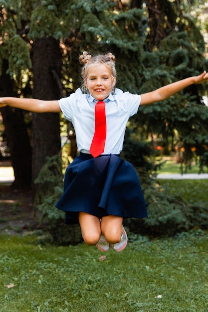 Colegiala feliz sosteniendo un libro al aire libre. Un niño pequeño va a la escuela. Copie el espacio.