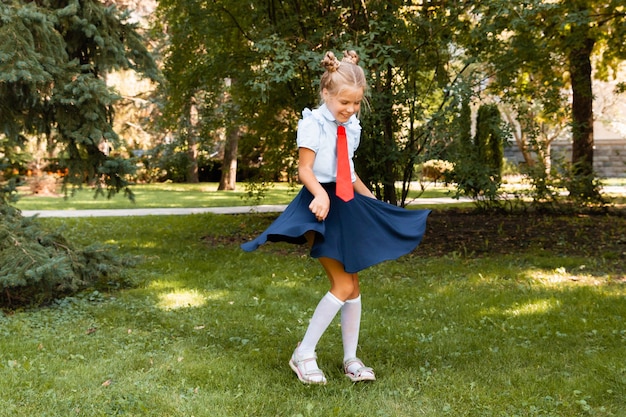 Colegiala feliz sosteniendo un libro al aire libre. Un niño pequeño va a la escuela. Copie el espacio.