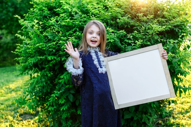 Colegiala feliz sosteniendo una pizarra blanca con espacio para texto Anuncio escolar del comienzo de la formación Regreso a la escuela