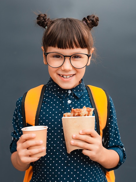 Colegiala con gafas en un descanso para almorzar sobre un fondo gris Comidas escolares comida rápida saludable para niños