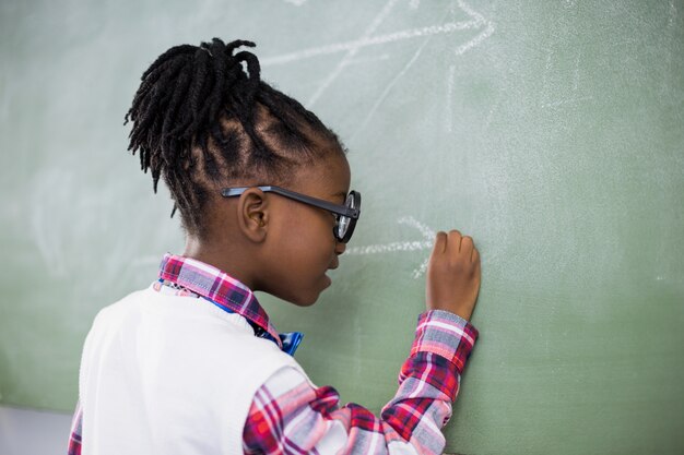 Colegiala haciendo matemáticas en la pizarra en el aula