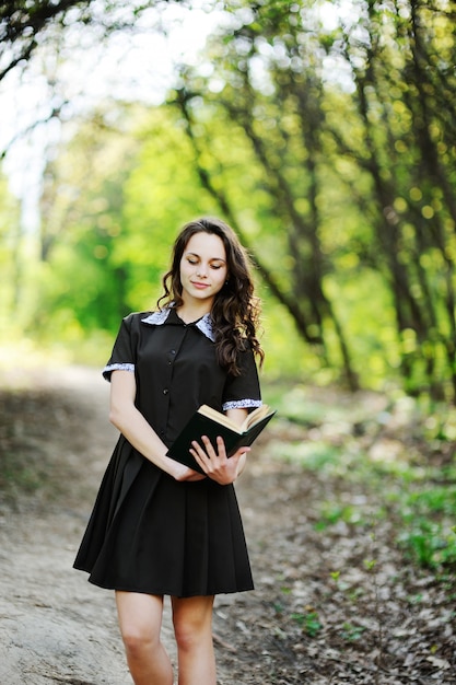 Colegiala hermosa con un libro en manos sobre un fondo de árboles verdes