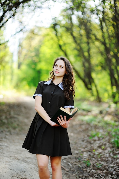 Foto colegiala hermosa con un libro en manos sobre un fondo de árboles verdes