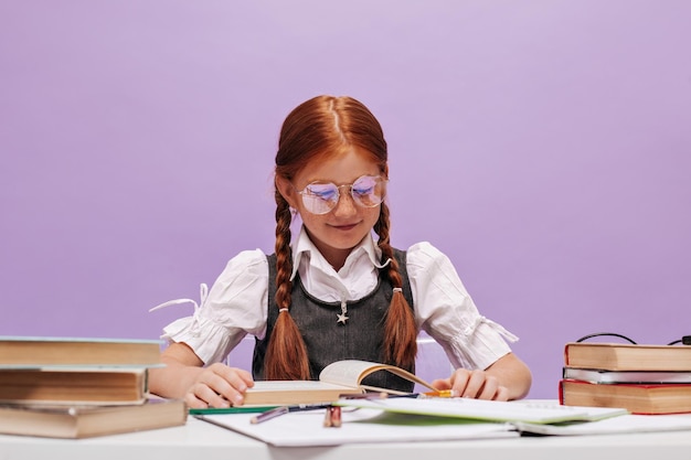 Foto colegiala joven alegre con dos coletas rojas y pecas lindas en uniforme moderno sonriendo y leyendo sobre fondo aislado