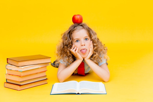 La colegiala lee un libro interesante sobre un fondo amarillo en el estudio. Manzana roja junto a los libros. concepto de escuela.