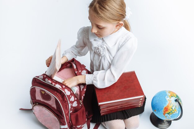 Colegiala linda niña sentada con libros y un globo, sonriente y feliz