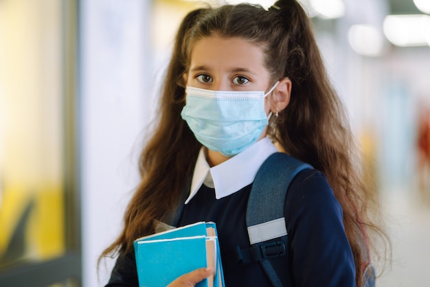 Colegiala con una máscara protectora con una mochila y un libro de texto.