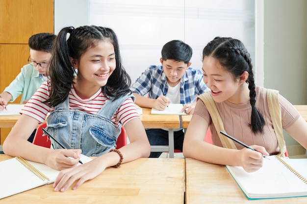 Colegiala mirando el cuaderno de su compañero de clase y tratando de copiar las respuestas de su examen