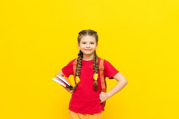 Una colegiala con una mochila y libros de texto Preparando a un estudiante para los exámenes Una niña va a la escuela con un fondo amarillo aislado Educación infantil