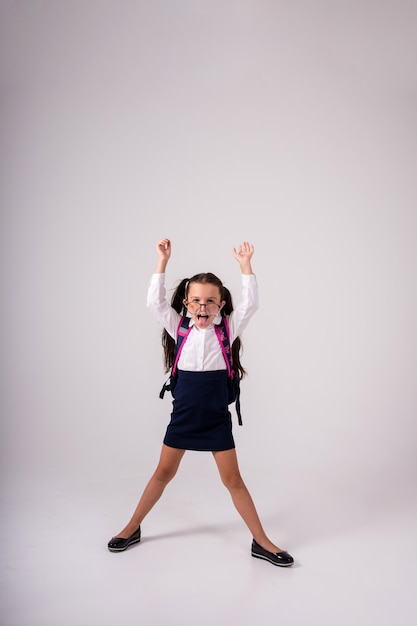 Una colegiala morena alegre en uniforme y gafas sobre un fondo blanco con un lugar para el texto