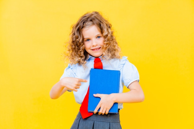 Colegiala de la muchacha del retrato del primer en fondo amarillo. Un niño de la escuela primaria sostiene un libro de texto y señala hacia arriba. Concepto de educación.
