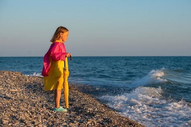 colegiala en un paseo por la orilla del mar en un impermeable y con un paraguas