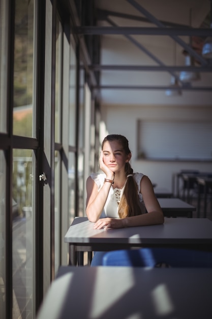 Colegiala pensativa sentada en el aula