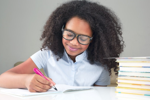 Colegiala de piel oscura con gafas escribe en un cuaderno. aprendizaje en la educación escolar