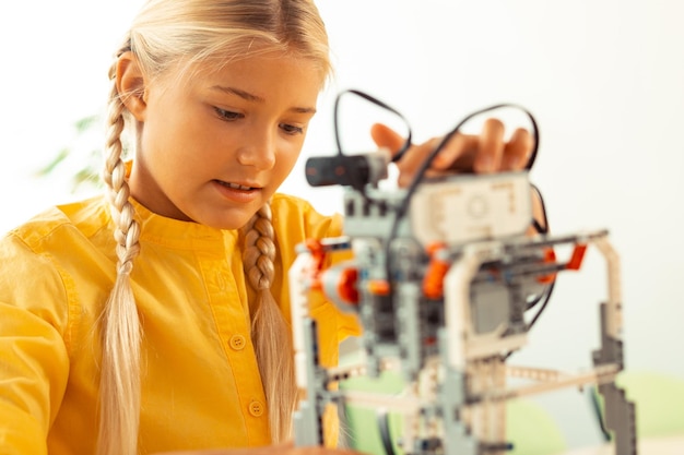 Colegiala de primaria enfocada jugando con un robot complicado que hizo usando un juego de construcción