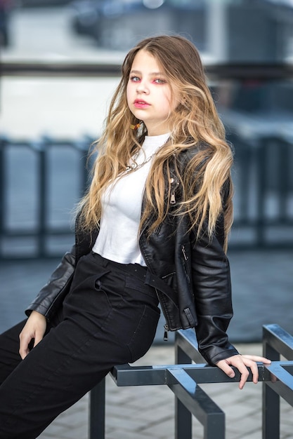 Colegiala rubia joven en chaqueta de cuero negro posando en el estacionamiento