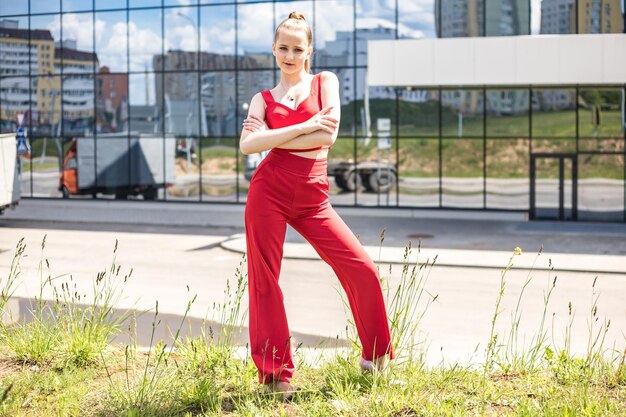 Colegiala rubia joven en un traje rojo y una chaqueta blanca posando en el estacionamiento