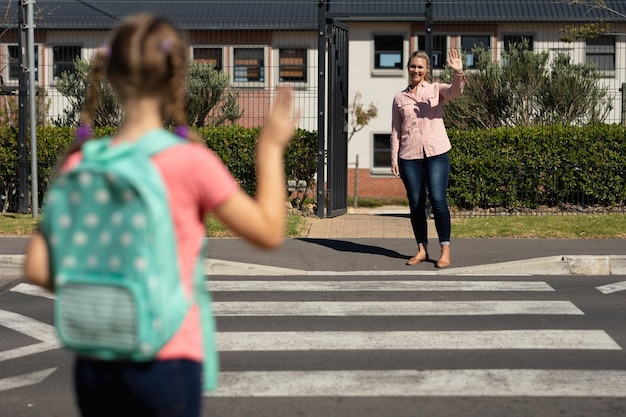 Foto colegiala saludando a su madre en un paso de peatones