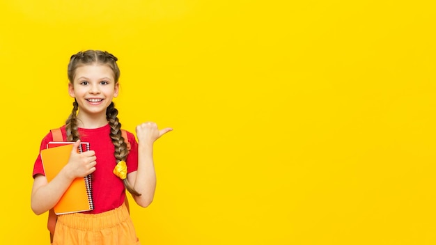 Una colegiala señala su anuncio sobre un fondo amarillo aislado Cursos de formación adicionales para escolares Una niña feliz señala el anuncio