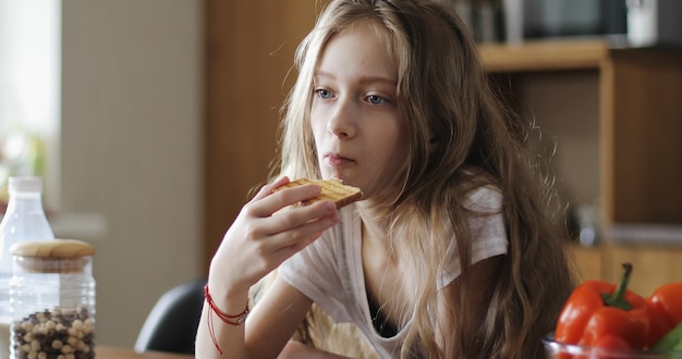 Colegiala seria con pelo largo come pan blanco Un niño come tostadas en la cocina