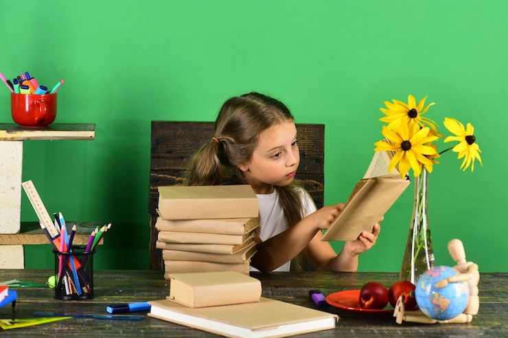Foto la colegiala se sienta en el escritorio con coloridos libros de papelería y flores.