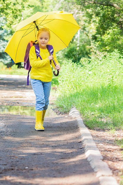 una colegiala de siete años, vestida de amarillo, va a la escuela bajo un paraguas con una mochila