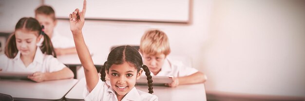 Colegiala sonriente levantando la mano en el aula