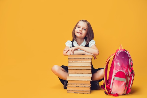 Colegiala sonriente sentada detrás de una pila de libros con mochila concepto de aprendizaje y escuela