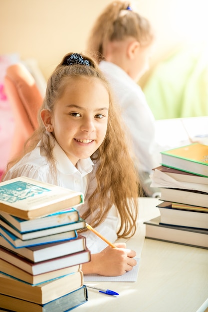 Colegiala sonriente sentado en la biblioteca y haciendo los deberes