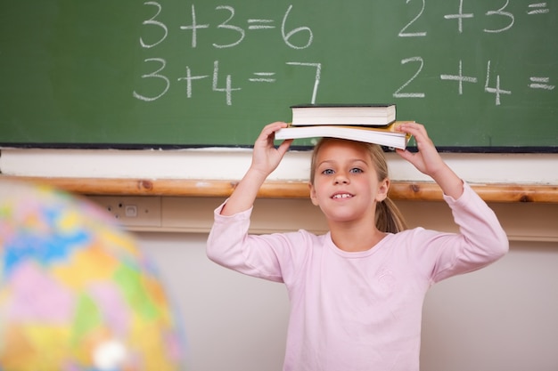 Colegiala sonriente sosteniendo su libro sobre su cabeza