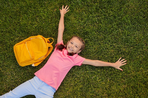 Colegiala sonriente tumbado sobre el césped durante las vacaciones