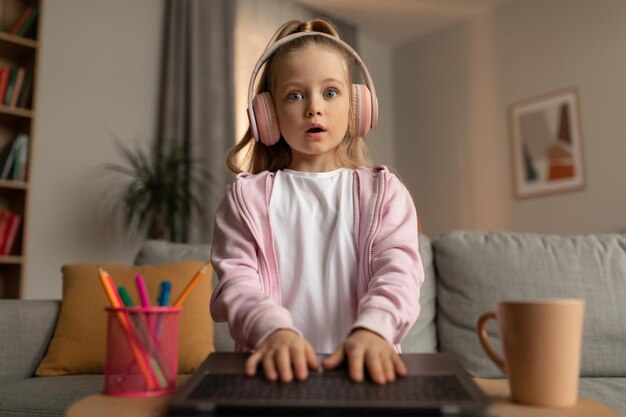 Colegiala sorprendida mirando la computadora portátil con auriculares en casa