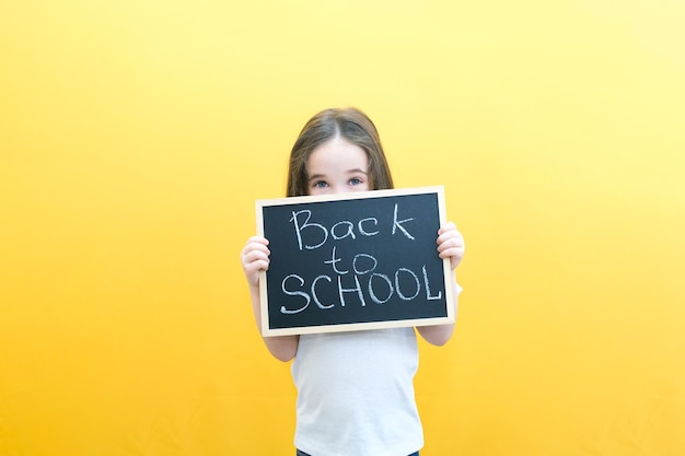 Colegiala sosteniendo una tableta en sus manos con la inscripción Regreso a la escuela en un fondo amarillo