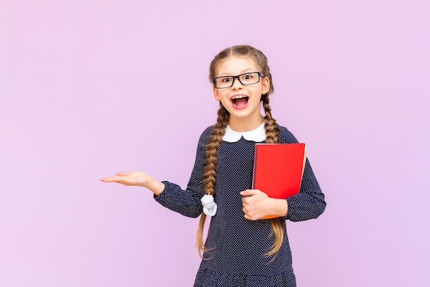 Una colegiala sostiene cuadernos y su anuncio en la palma de un fondo rosa aislado Cursos educativos para niños de secundaria