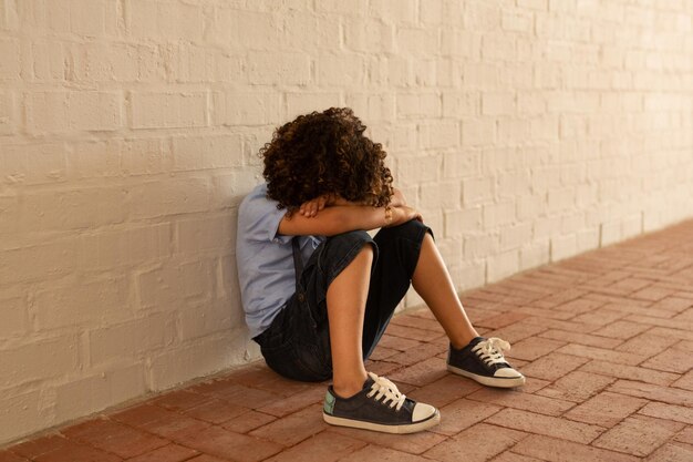 Una colegiala triste sentada sola en el suelo en el pasillo.