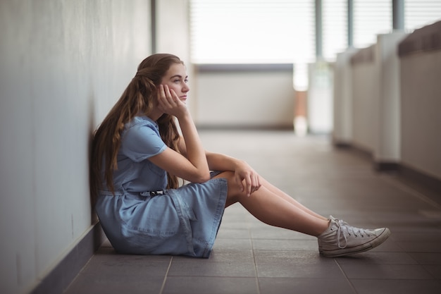 Foto colegiala triste sentado en el pasillo