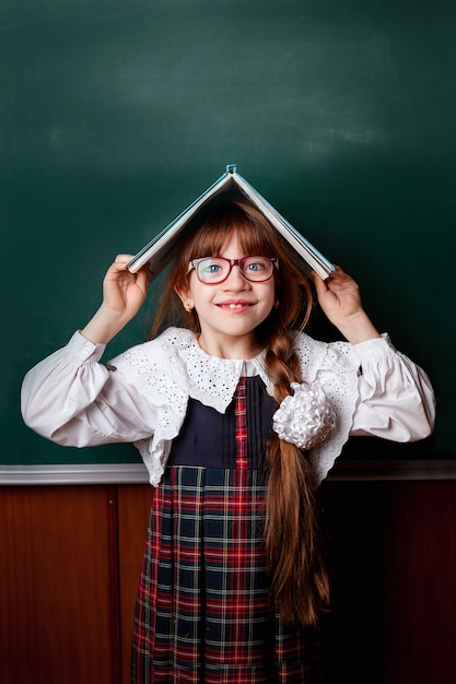 Colegiala en uniforme escolar con un libro en la cabeza