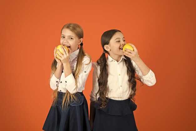 Las colegialas comen manzanas Almuerzo escolar Nutrición vitamínica durante el día escolar Impulsar la aceptación de la fruta por parte de los estudiantes Distribuir fruta fresca gratis en la escuela Niñas niños uniforme escolar fondo naranja