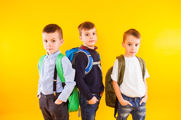 Colegiales lindos en uniforme con mochilas sobre fondo amarillo Regreso a la escuela