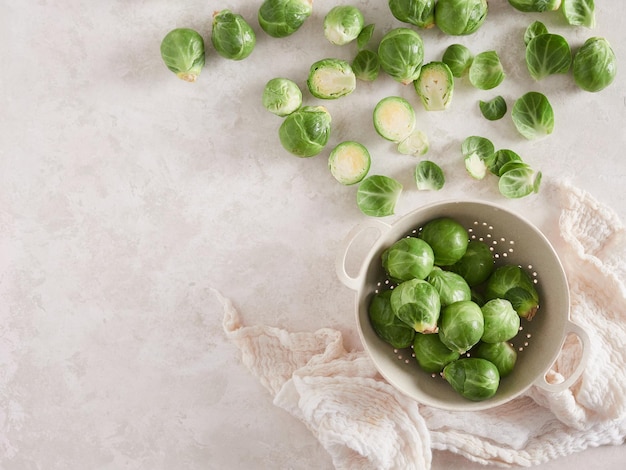 Coles de bruselas crudas en un colador varias esparcidas en el mostrador de la cocina con algunas hojas despojadas de la vista superior con espacio para copiar